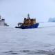 An icebreaker makes the path for a cargo ship with an iceberg in the background near a port on the Alexandra Land island near Nagurskoye, Russia.